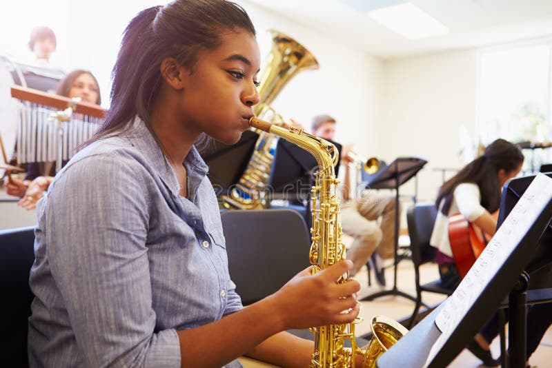 Θηλυκός μαθητής που παίζει Saxophone στην ορχήστρα γυμνασίου στοκ φωτογραφία με δικαίωμα ελεύθερης χρήσης Θηλυκός μαθητής που παίζει Saxophone στην ορχήστρα γυμνασίου στοκ φωτογραφία με δικαίωμα ελεύθερης χρήσης