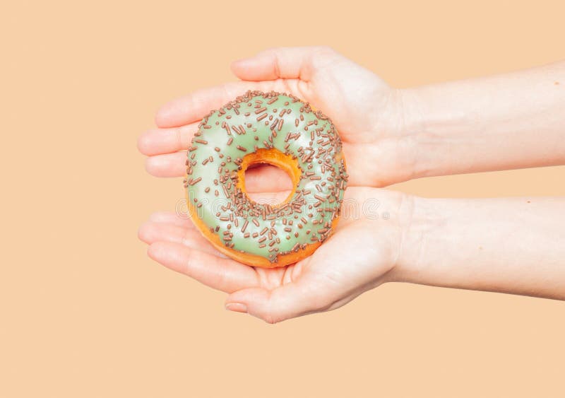 Θηλυκά χέρια που κρατούν ζωηρόχρωμο doughnut στο υπόβαθρο κρητιδογραφιών στοκ εικόνα Θηλυκά χέρια που κρατούν ζωηρόχρωμο doughnut στο υπόβαθρο κρητιδογραφιών στοκ εικόνα