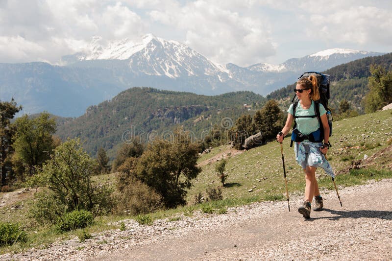Θηλυκό backpacker που περπατά κάτω από το δρόμο στους λόφους στοκ εικόνα με δικαίωμα ελεύθερης χρήσης Θηλυκό backpacker που περπατά κάτω από το δρόμο στους λόφους στοκ εικόνα με δικαίωμα ελεύθερης χρήσης