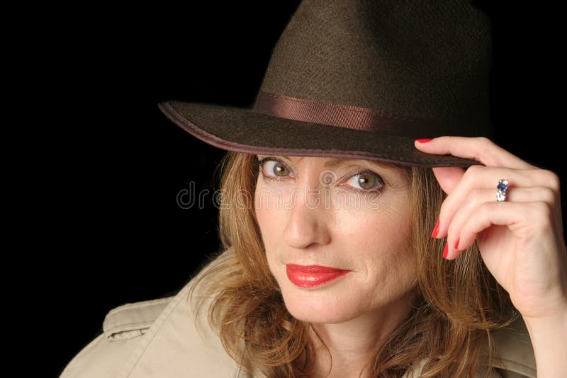 A beautiful woman in a smiling in a hat and trenchcoat over a black background. Possible marital role playing. A beautiful woman in a smiling in a hat and trenchcoat over a black background. Possible marital role playing.