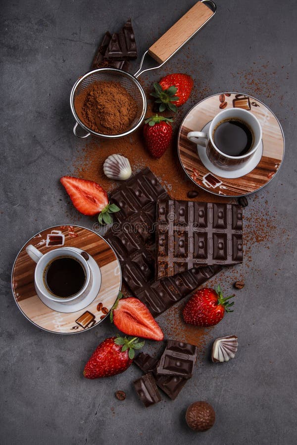 Broken chocolate blocks with strawberries and 2 cups of coffee on a gray background. Broken chocolate blocks with strawberries and 2 cups of coffee on a gray background