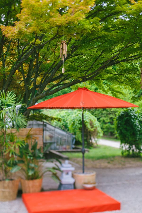 Japanese wind chimes wooden bamboo bells handed on tree in Japanese garden with red umbrella and potteries - tilt-shift lens focus effect. Japanese wind chimes wooden bamboo bells handed on tree in Japanese garden with red umbrella and potteries - tilt-shift lens focus effect