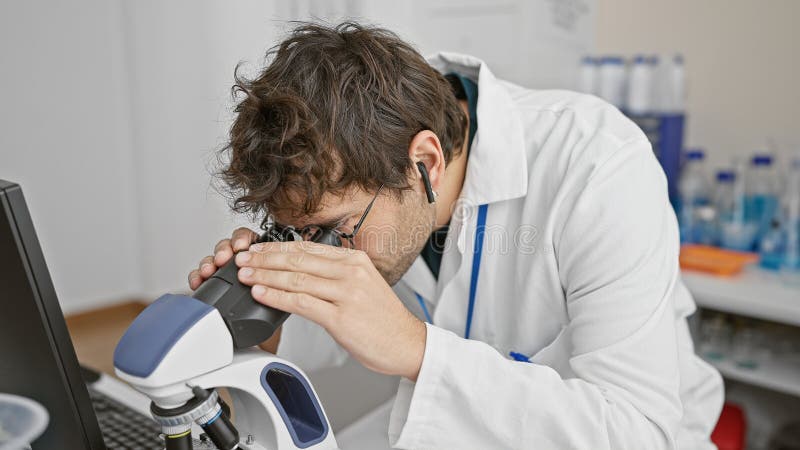 ισπανικός άνδρας με μούσι χρησιμοποιώντας μικροσκόπιο σε σύγχρονο εργαστήριο που παρουσιάζει ιατρική έρευνα σε εσωτερικούς χώρους στοκ φωτογραφία με δικαίωμα ελεύθερης χρήσης