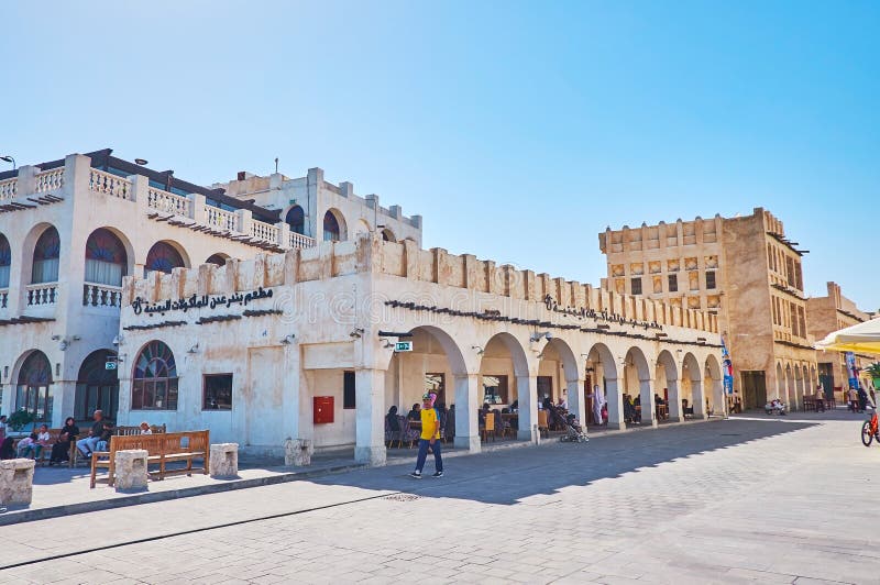 DOHA, QATAR - FEBRUARY 13, 2018: The central shopping street of Souq Waqif, restored old buildings have arcades, occupied with outdoor cafes and souvenir stores, on February 13 in Doha. DOHA, QATAR - FEBRUARY 13, 2018: The central shopping street of Souq Waqif, restored old buildings have arcades, occupied with outdoor cafes and souvenir stores, on February 13 in Doha.