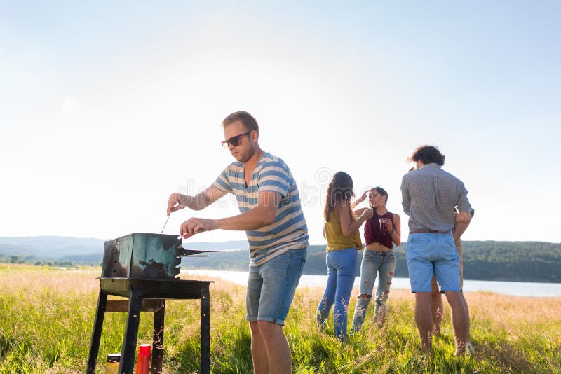 Κλίκα των νέων που κατασκευάζουν BBQ στη λίμνη στοκ εικόνες με δικαίωμα ελεύθερης χρήσης Κλίκα των νέων που κατασκευάζουν BBQ στη λίμνη στοκ εικόνες με δικαίωμα ελεύθερης χρήσης