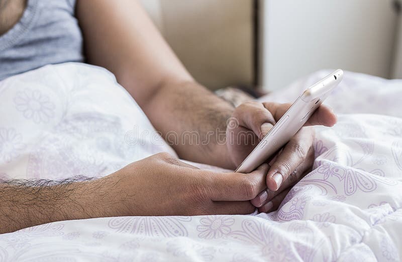 Κλείστε επάνω των νέων αρσενικών δάχτυλων χεριών που λειτουργούν στο κρεβάτι στο κινητό τηλέφωνο δακτυλογραφώντας sms στο πληκτρο στοκ φωτογραφία