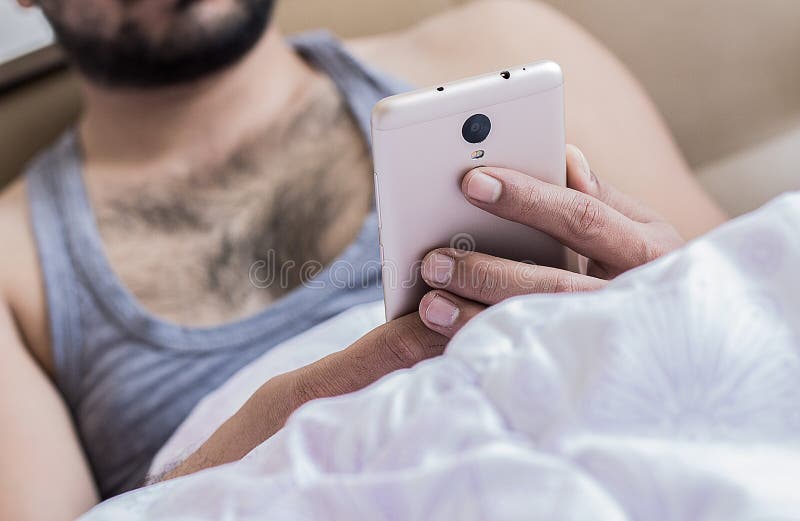 Κλείστε επάνω των νέων αρσενικών δάχτυλων χεριών που λειτουργούν στο κρεβάτι στο κινητό τηλέφωνο δακτυλογραφώντας sms στο πληκτρο στοκ εικόνες