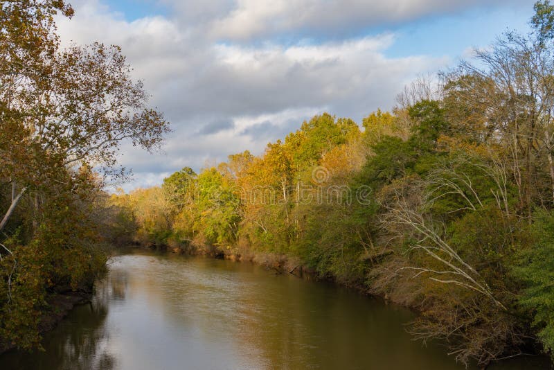 A bend in the Neuse River in Raleigh, North Carolina in autumn with the sun shining on the orange leaves of the trees; landscape view. A bend in the Neuse River in Raleigh, North Carolina in autumn with the sun shining on the orange leaves of the trees; landscape view