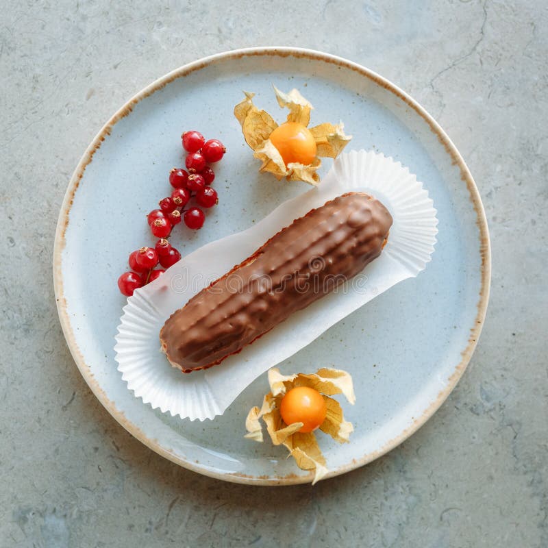 Κέικ ECLAIR σε ένα πιάτο με τη χρυσή περιποίηση που διακοσμείται με τα εσπεριδοειδή και τα μούρα στοκ φωτογραφία με δικαίωμα ελεύθερης χρήσης Κέικ ECLAIR σε ένα πιάτο με τη χρυσή περιποίηση που διακοσμείται με τα εσπεριδοειδή και τα μούρα στοκ φωτογραφία με δικαίωμα ελεύθερης χρήσης