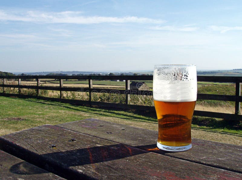 A pint of English Beer on a typical pub beer garden table, overlooking a typical english countryside landscape. A pint of English Beer on a typical pub beer garden table, overlooking a typical english countryside landscape.