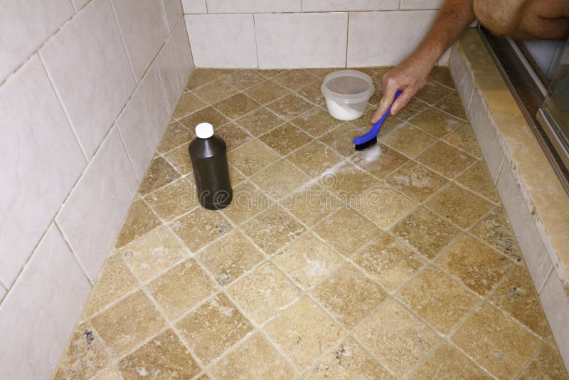 Adult male hand with a small blue and black brush cleaning floor grout in a shower. White male cleaning shower grout with hydrogen peroxide and baking soda. Adult male hand with a small blue and black brush cleaning floor grout in a shower. White male cleaning shower grout with hydrogen peroxide and baking soda.