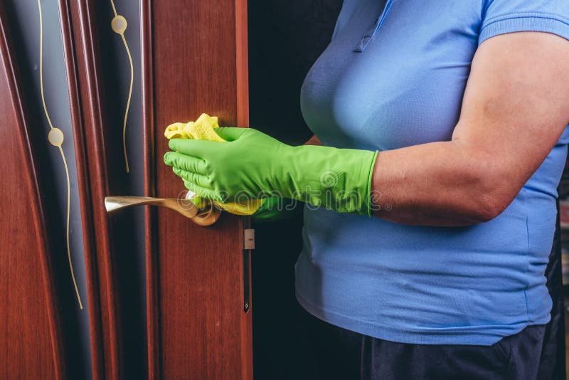καθαρισμός στο σπίτι. ένα κορίτσι με πράσινα γάντια σβήνει την πόρτα του δέντρου και τη μεταλλική λαβή της πόρτας με κίτρινο πανί.