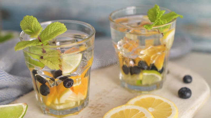 Summer healthy cocktails of citrus infused waters, lemonades or mojitos, with lime lemon orange blueberries and mint, diet detox beverages, in glasses on light background. Summer healthy cocktails of citrus infused waters, lemonades or mojitos, with lime lemon orange blueberries and mint, diet detox beverages, in glasses on light background