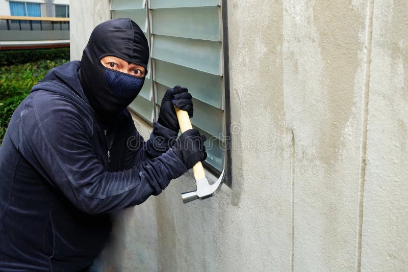 Καλυμμένος κλέφτης που χρησιμοποιεί ένα σφυρί που προσπαθεί να σπάσει τα παράθυρα στοκ φωτογραφίες Καλυμμένος κλέφτης που χρησιμοποιεί ένα σφυρί που προσπαθεί να σπάσει τα παράθυρα στοκ φωτογραφίες