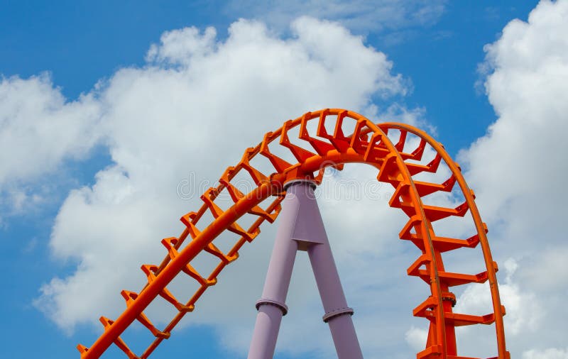 A Curved of orange Roller Coaster track in close up isolated on cloudy blue sky background. A Curved of orange Roller Coaster track in close up isolated on cloudy blue sky background.