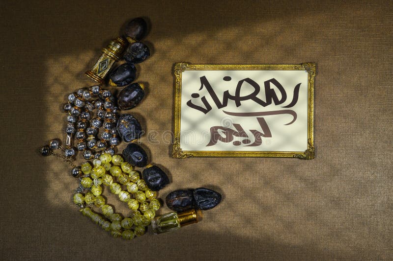 Date fruits and rosary muslim and Oud perfume arranged in moon shape and gold frame with arabic text meaning happy ramadan in english, shadow window. Islamic festive food and it's significance. Date fruits and rosary muslim and Oud perfume arranged in moon shape and gold frame with arabic text meaning happy ramadan in english, shadow window. Islamic festive food and it's significance
