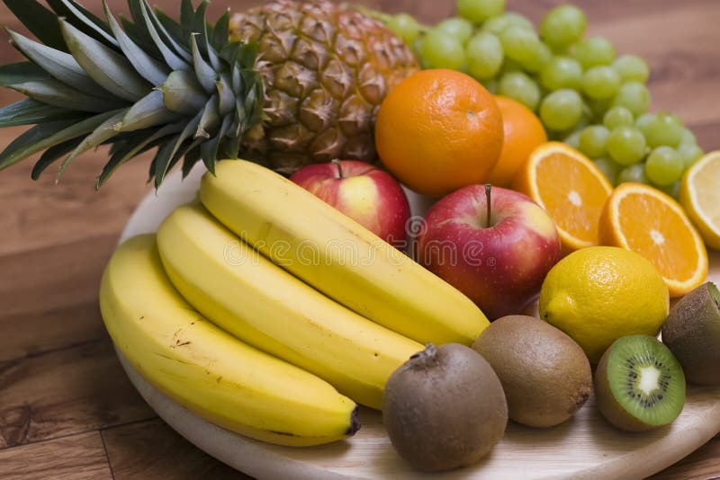 Colourful composition arranged on wooden chopping board, consisting of fresh fruit. The ingredients are: pineapple, bananas, kiwis, grapes, oranges. Colourful composition arranged on wooden chopping board, consisting of fresh fruit. The ingredients are: pineapple, bananas, kiwis, grapes, oranges.