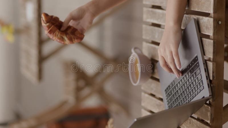 κατακόρυφη φωτογραφία μιας γυναίκας να πληκτρολογεί στο φορητό υπολογιστή με πρωινό κρουασάν και τσάι σε εξωτερικό χώρο φιλμ μικρού μήκους