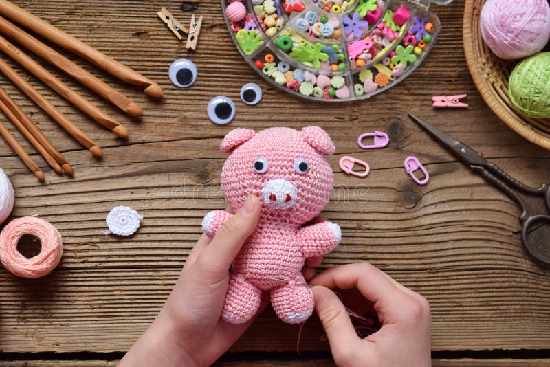 Making pink pig. Crochet toy for child. On table threads, needles, hook, cotton yarn. Step 2 - to sew all details of toy. Handmade crafts. DIY concept. Small business. Income from hobby. Making pink pig. Crochet toy for child. On table threads, needles, hook, cotton yarn. Step 2 - to sew all details of toy. Handmade crafts. DIY concept. Small business. Income from hobby