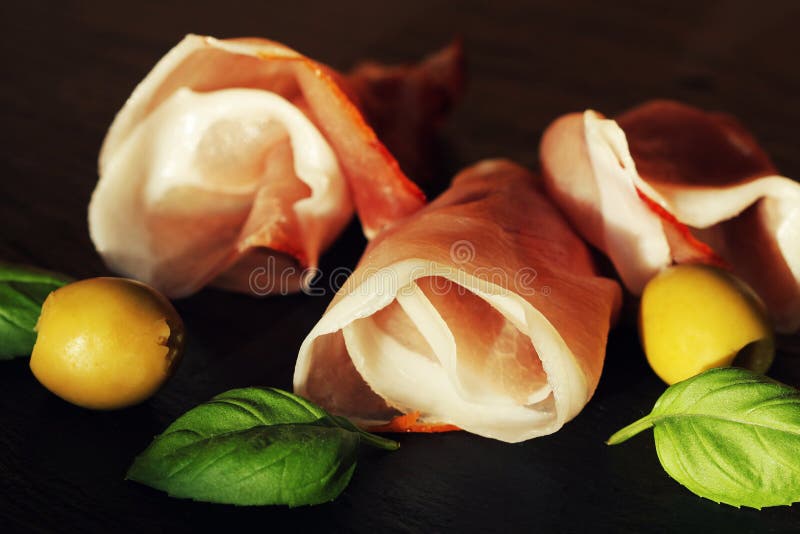Κατσαρωμένες φέτες εύγευστου Prosciutto με τα φύλλα και τις ελιές βασιλικού στοκ εικόνες με δικαίωμα ελεύθερης χρήσης Κατσαρωμένες φέτες εύγευστου Prosciutto με τα φύλλα και τις ελιές βασιλικού στοκ εικόνες με δικαίωμα ελεύθερης χρήσης