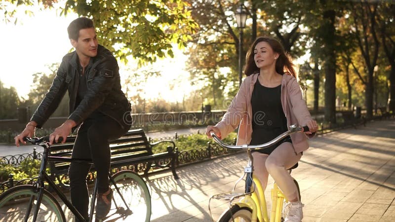Καυκάσιοι νέοι ζεύγος ή φίλοι που οδηγά τα ποδήλατά τους στο κενή πάρκο ή τη λεωφόρο πόλεων στο καλοκαίρι Ομιλία σε κάθε ένας
