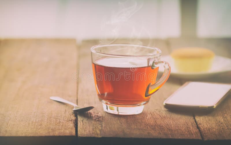 Καυτό φλυτζάνι τσαγιού με το βουτύρου κέικ και smartpho στον πίνακα στα WI στοκ φωτογραφία με δικαίωμα ελεύθερης χρήσης Καυτό φλυτζάνι τσαγιού με το βουτύρου κέικ και smartpho στον πίνακα στα WI στοκ φωτογραφία με δικαίωμα ελεύθερης χρήσης