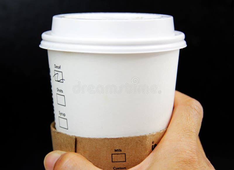 Hand holding a commercial cup with lid on with a blank space against a black background. Hand holding a commercial cup with lid on with a blank space against a black background.