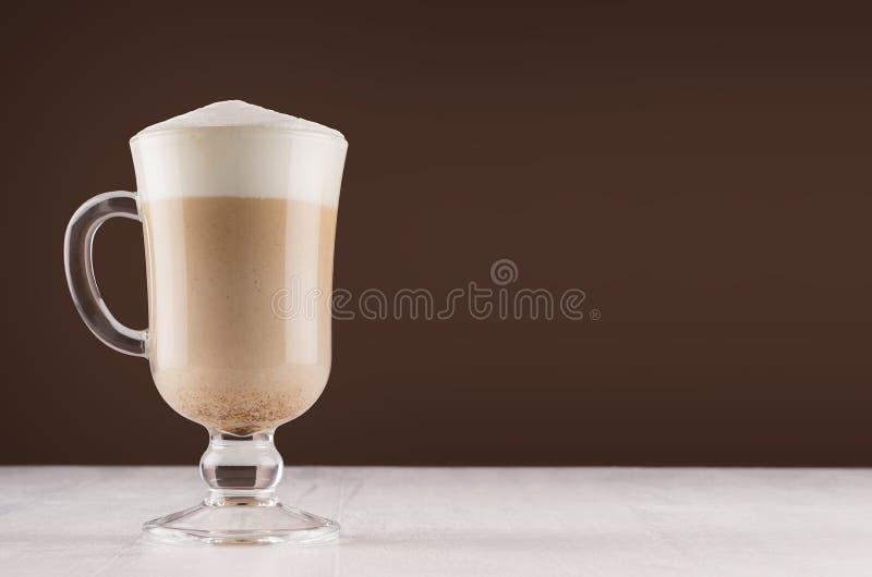 Καφές Cappuccino στο κομψό γυαλί με τον αφρό στον άσπρο πίνακα και το σκοτεινό καφετή τοίχο, διάστημα αντιγράφων στοκ φωτογραφία με δικαίωμα ελεύθερης χρήσης