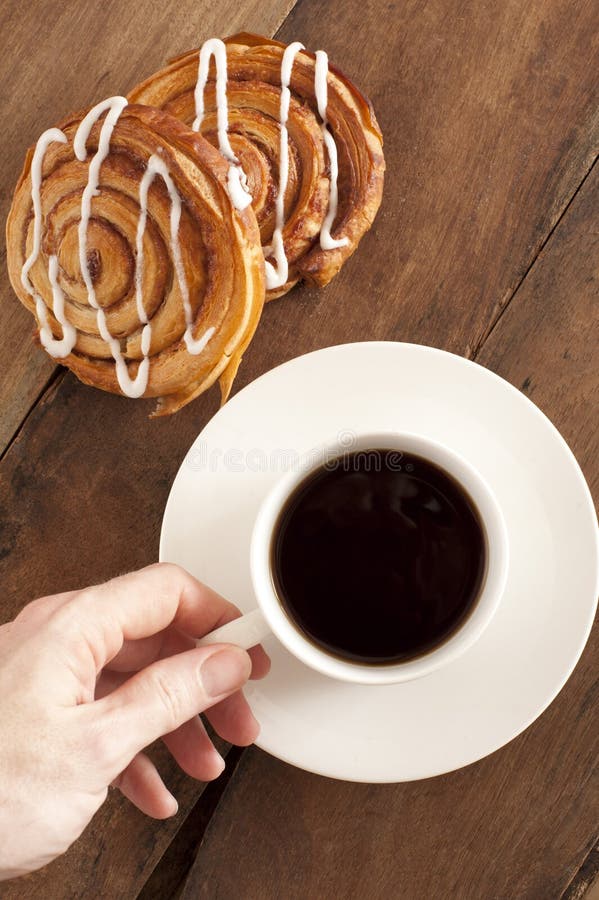 Overhead view of a mans hand reaching out to take a cup of rich espresso coffee and fresh Danish pastries for breakfast. Overhead view of a mans hand reaching out to take a cup of rich espresso coffee and fresh Danish pastries for breakfast