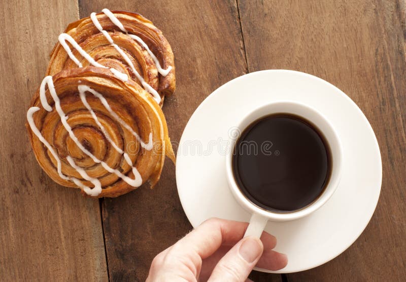 Man reaching for a cup and saucer of full roast espresso coffee with fresh Danish pastries for a refreshing coffee break, high angle view on wood. Man reaching for a cup and saucer of full roast espresso coffee with fresh Danish pastries for a refreshing coffee break, high angle view on wood