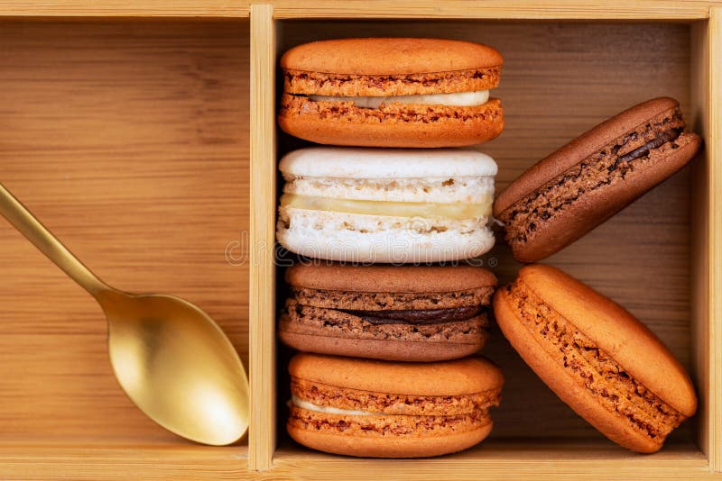 Καφετιά και άσπρα γαλλικά macarons ή macaroons, που συσσωρεύονται σε ένα κιβώτιο μπαμπού με το χρυσό κουτάλι στοκ εικόνες Καφετιά και άσπρα γαλλικά macarons ή macaroons, που συσσωρεύονται σε ένα κιβώτιο μπαμπού με το χρυσό κουτάλι στοκ εικόνες
