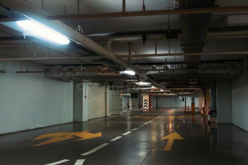 Κενός διάδρομος στο φωτισμένο υπόγειο εσωτερικό χώρων στάθμευσης αυτοκινήτων κάτω από τη σύγχρονη λεωφόρο με τα βέλη στο πάτωμα στοκ εικόνα Κενός διάδρομος στο φωτισμένο υπόγειο εσωτερικό χώρων στάθμευσης αυτοκινήτων κάτω από τη σύγχρονη λεωφόρο με τα βέλη στο πάτωμα στοκ εικόνα