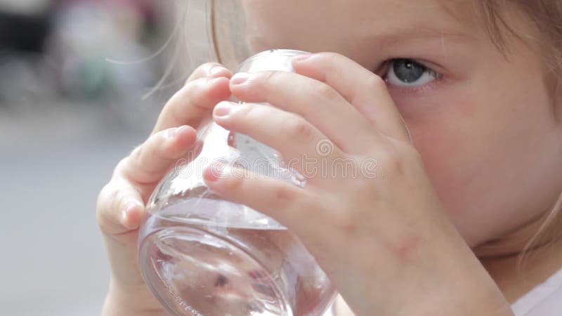 Κινηματογράφηση σε πρώτο πλάνο του λίγο χαριτωμένου κοριτσιού που πίνει το καθαρό νερό από ένα γυαλί