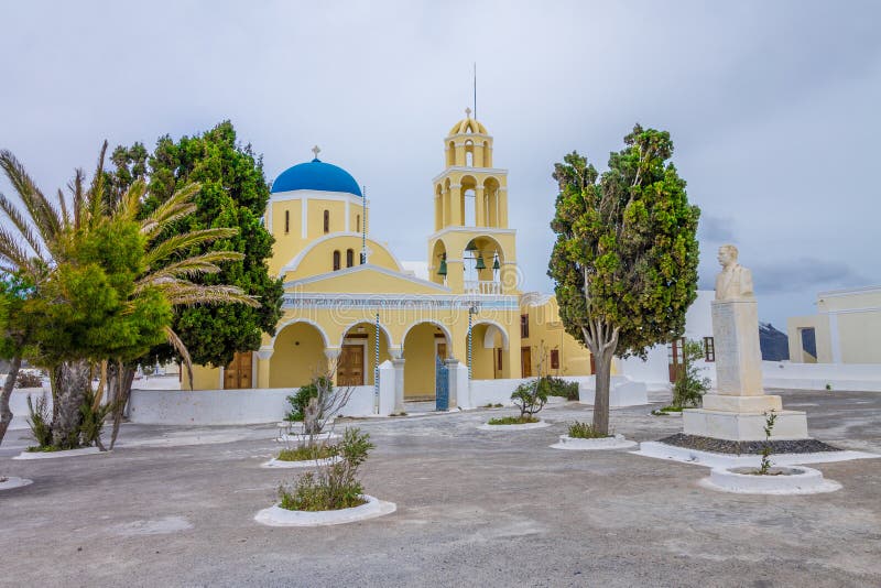 κλασική ελληνική ορθόδοξη εκκλησία στη νήσο αγία σαντορίνη. όμορφη κίτρινη εκκλησία με μπλε θόλο σε μια πλατεία σε συννεφιά. στοκ φωτογραφία