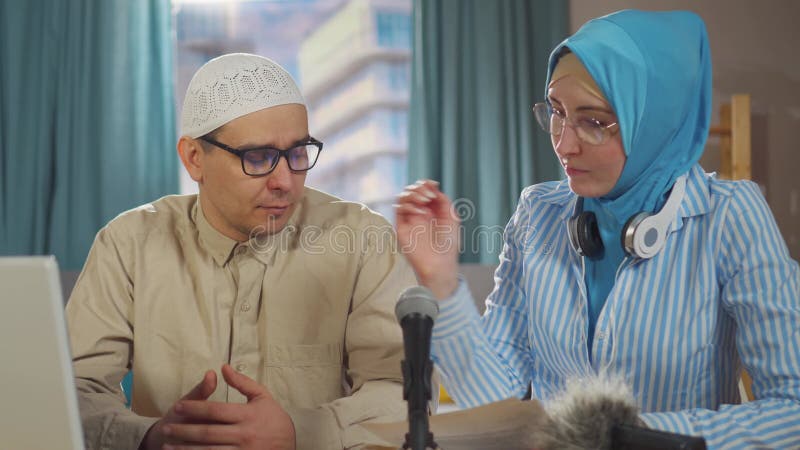 κλείσιμο νεαρής μουσουλμάνας και μουσουλμάνου άνδρα καταγράφουν podcast συνέντευξης ενώ κάθονται μπροστά από ένα μικρόφωνο στο