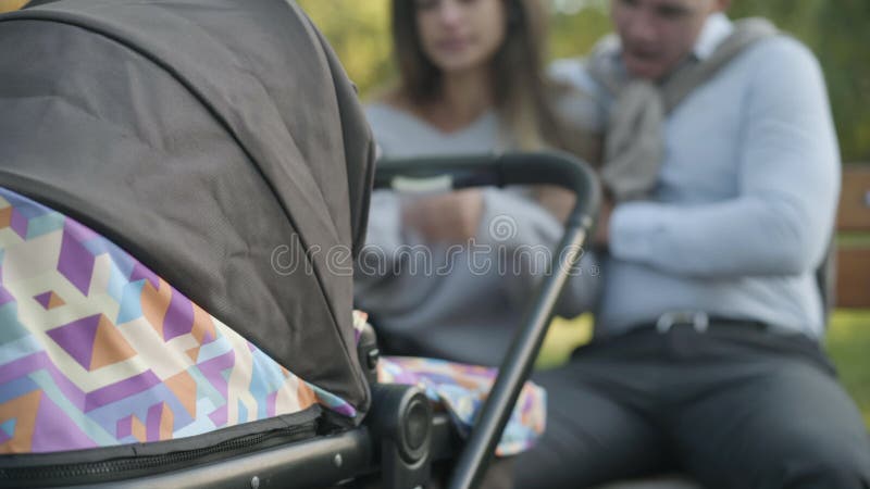 κλείσιμο της μεταφοράς μωρών με θαμπό ζευγάρι νεαρών κουρασμένων γονιών να χαμογελά και να αγκαλιάζει καθισμένοι στο παρασκήνιο απόθεμα βίντεο