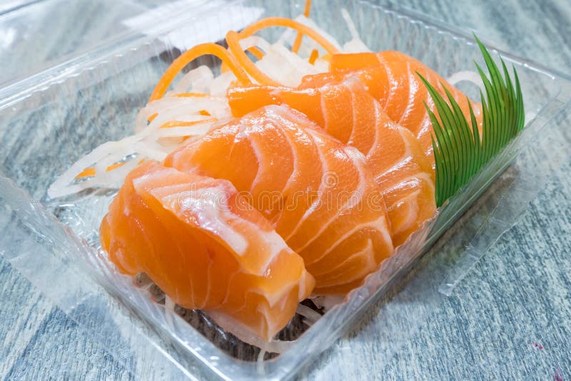 Κλείστε επάνω του ακατέργαστου sashimi σολομών πακέτου στο σαφές πλαστικό κιβώτιο στον ξύλινο πίνακα στοκ φωτογραφία με δικαίωμα ελεύθερης χρήσης Κλείστε επάνω του ακατέργαστου sashimi σολομών πακέτου στο σαφές πλαστικό κιβώτιο στον ξύλινο πίνακα στοκ φωτογραφία με δικαίωμα ελεύθερης χρήσης