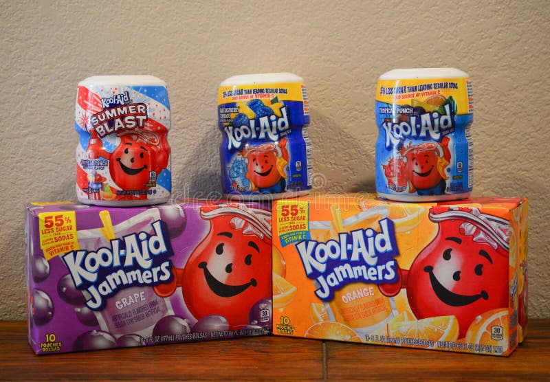 Two Tropical Punch, one Blue Raspberry Lemonade, one grape and one orange Kool-Aid drink powder mix and Kool-Aid Jammers on a wooden table and an off white background. Two Tropical Punch, one Blue Raspberry Lemonade, one grape and one orange Kool-Aid drink powder mix and Kool-Aid Jammers on a wooden table and an off white background