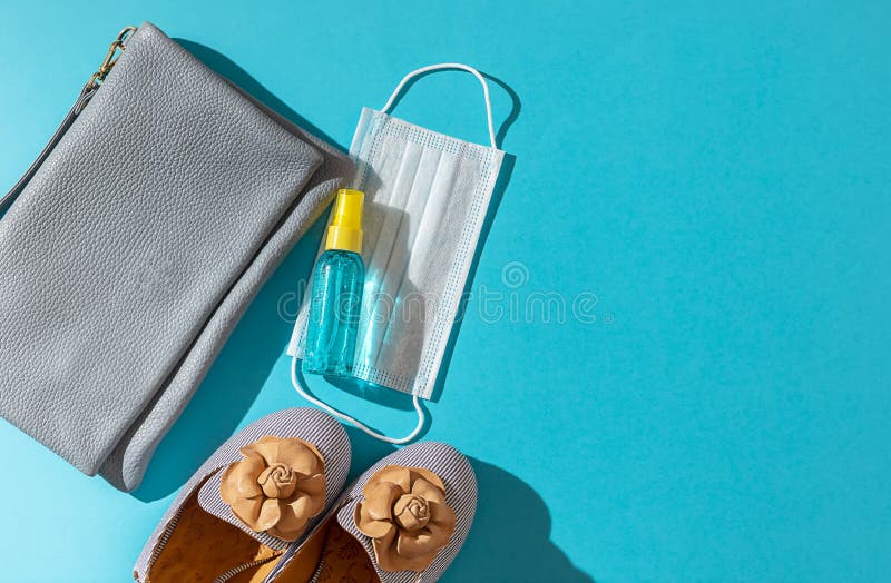 Stylish female shoes and Leather bag out with face mask ,sanitizer hand gel to protect from Coronavirus or COVID-19 on a blue background with sunlight shadow. Copy space, flat lay. Stylish female shoes and Leather bag out with face mask ,sanitizer hand gel to protect from Coronavirus or COVID-19 on a blue background with sunlight shadow. Copy space, flat lay