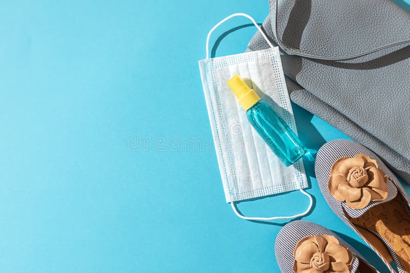 Stylish female shoes and Leather bag out with face mask ,sanitizer hand gel to protect from Coronavirus or COVID-19 on a blue background with sunlight shadow. Copy space, flat lay. Stylish female shoes and Leather bag out with face mask ,sanitizer hand gel to protect from Coronavirus or COVID-19 on a blue background with sunlight shadow. Copy space, flat lay