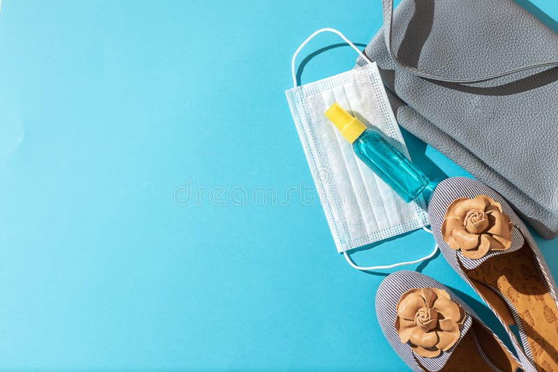 Stylish female shoes and Leather bag out with face mask ,sanitizer hand gel to protect from Coronavirus or COVID-19 on a blue background with sunlight shadow. Copy space, flat lay. Stylish female shoes and Leather bag out with face mask ,sanitizer hand gel to protect from Coronavirus or COVID-19 on a blue background with sunlight shadow. Copy space, flat lay