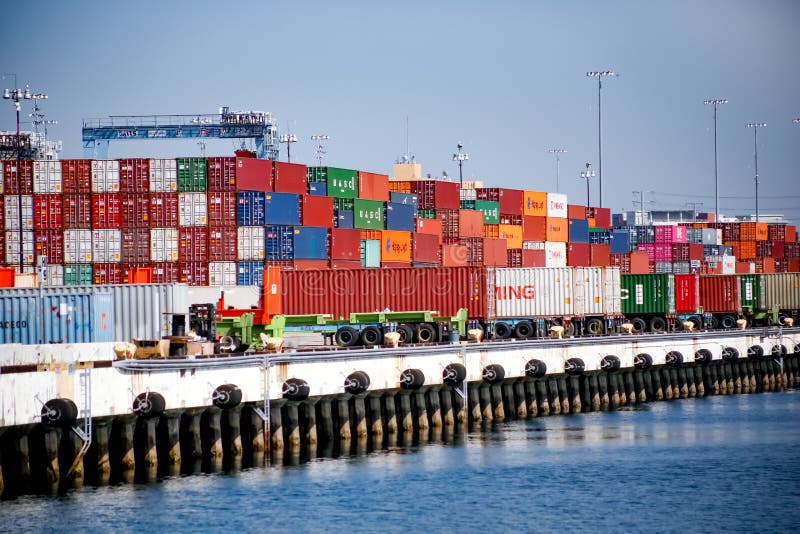 A view of several stacks of shipping containers. Some shipping containers are on truck beds on the dock. Seen in the Port of Long Beach, in California. A view of several stacks of shipping containers. Some shipping containers are on truck beds on the dock. Seen in the Port of Long Beach, in California.