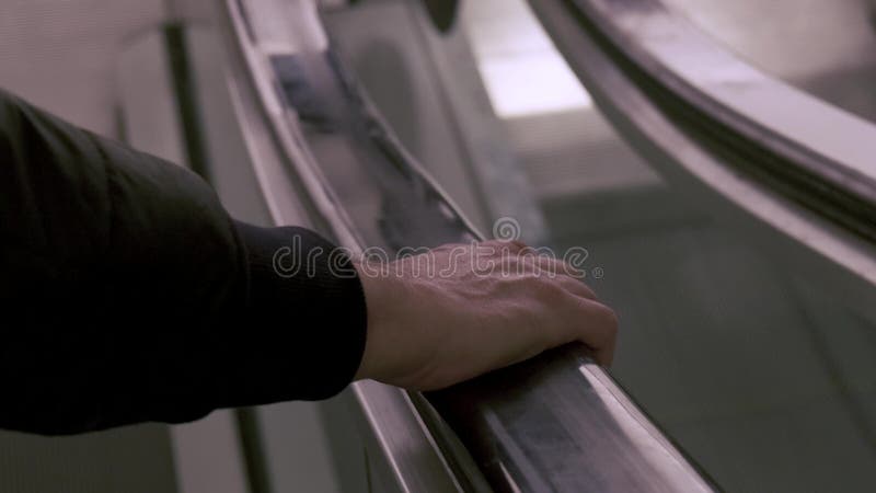 κοντινό πλάνο ανδρικού χεριού σε μαύρη ελαστική χειρολισθήρα μιας κυλιόμενης σκάλας ενώ μετακινείται προς τα κάτω. φιλμ μικρού μήκους