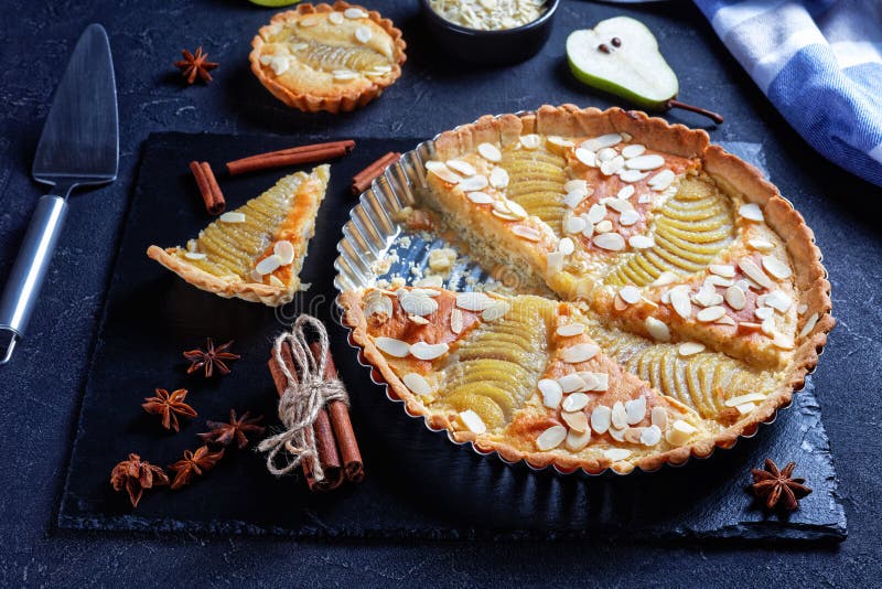 Close-up of classic french Pear Tart, La Tarte Bourdaloue filled with poached pears and frangipane cream served on a black stone board on a concrete table, view from above. Close-up of classic french Pear Tart, La Tarte Bourdaloue filled with poached pears and frangipane cream served on a black stone board on a concrete table, view from above