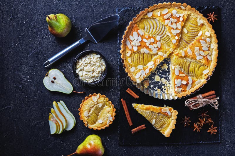 Close-up of sliced French Pear Tart, La Tarte Bourdaloue filled with poached pears and frangipane cream served on a black stone board on a concrete table, horizontal view from above, flatlay. Close-up of sliced French Pear Tart, La Tarte Bourdaloue filled with poached pears and frangipane cream served on a black stone board on a concrete table, horizontal view from above, flatlay