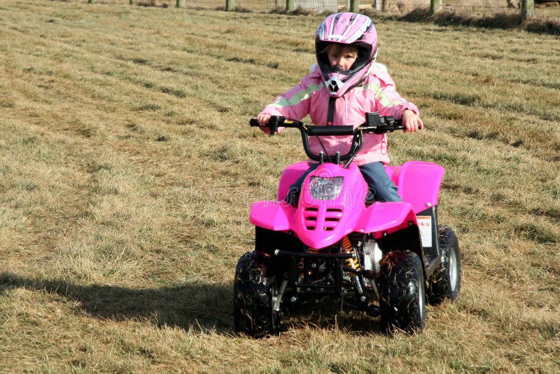 A little girl riding a pink four wheeler quad in her backyard. A little girl riding a pink four wheeler quad in her backyard.