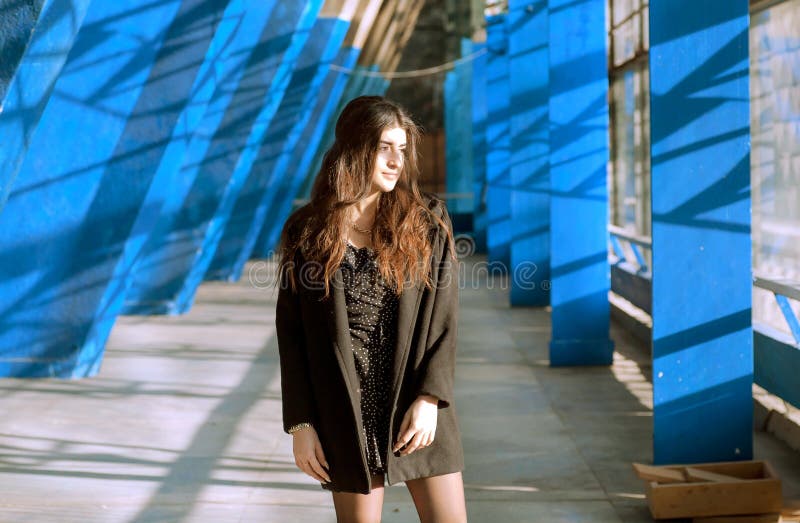Κορίτσι brunette Smily που στέκεται μεταξύ των μπλε τοίχων της περιοχής πόλεων grunge Νέα γυναίκα που φαίνεται καλή στο αστικό εσ