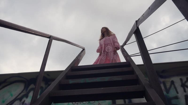 κορίτσι με ένα φόρεμα στην κορυφή της μεταλλικής σκάλας κοιτάζει τριγύρω για να δει αν υπάρχει κανείς