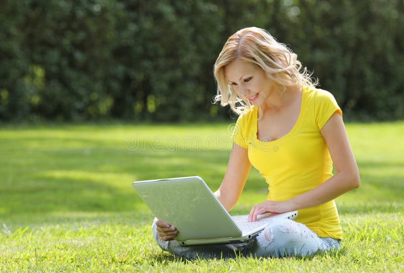 Κορίτσι με το lap-top. Ξανθή όμορφη νέα γυναίκα με τη συνεδρίαση σημειωματάριων στη χλόη. Υπαίθριος. Ηλιόλουστη ημέρα στοκ εικόνα Κορίτσι με το lap-top. Ξανθή όμορφη νέα γυναίκα με τη συνεδρίαση σημειωματάριων στη χλόη. Υπαίθριος. Ηλιόλουστη ημέρα στοκ εικόνα