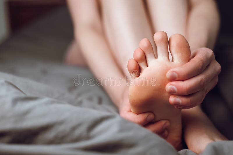 Tired female feeling discomfort rubbing her sore and painful foot and toes, during exercise sitting on bed at home. Woman foot massage to relieve pain from ache. Tense sore sprained muscle. Tired female feeling discomfort rubbing her sore and painful foot and toes, during exercise sitting on bed at home. Woman foot massage to relieve pain from ache. Tense sore sprained muscle